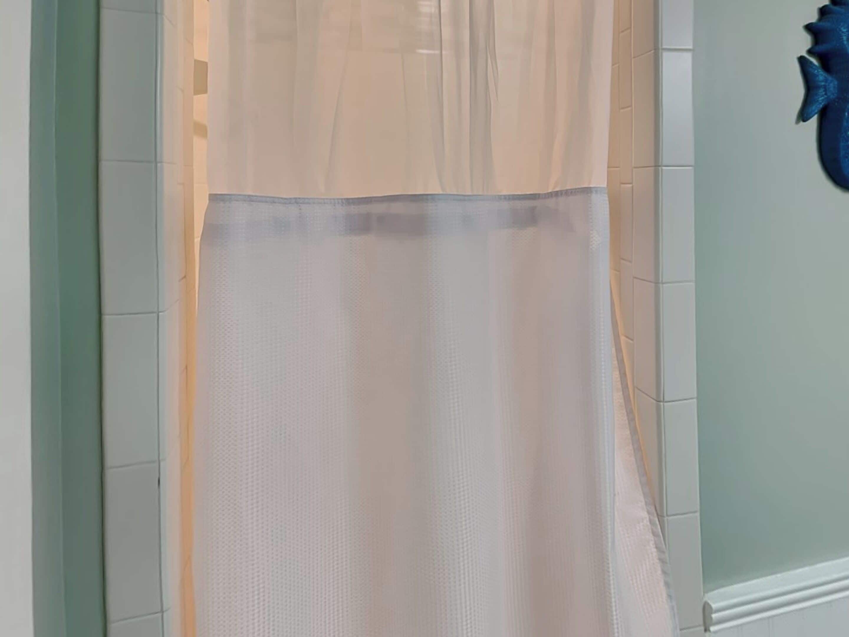 Ein Badezimmer mit Duschvorhang, gefliesten Wänden und einem blauen Dekorationselement an der Wand.