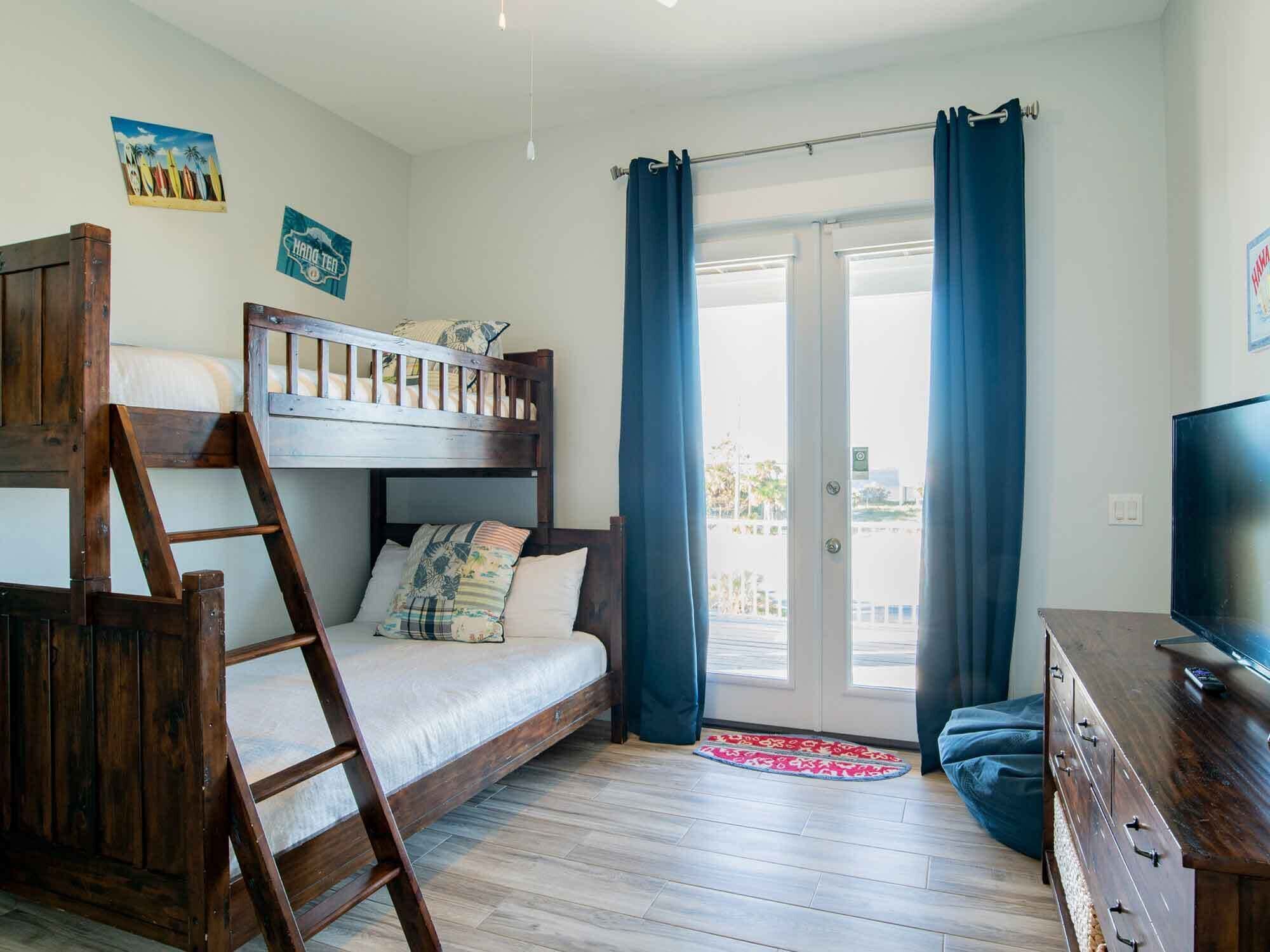 Una habitación con literas, un escritorio, un televisor y una puerta corredera de vidrio con cortinas.