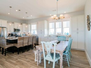 A spacious kitchen with white cabinetry, a central island with bar stools, and a dining table with chairs. - She Sells Seashells by Southern Vacation Rentals (Pensacola Beach)