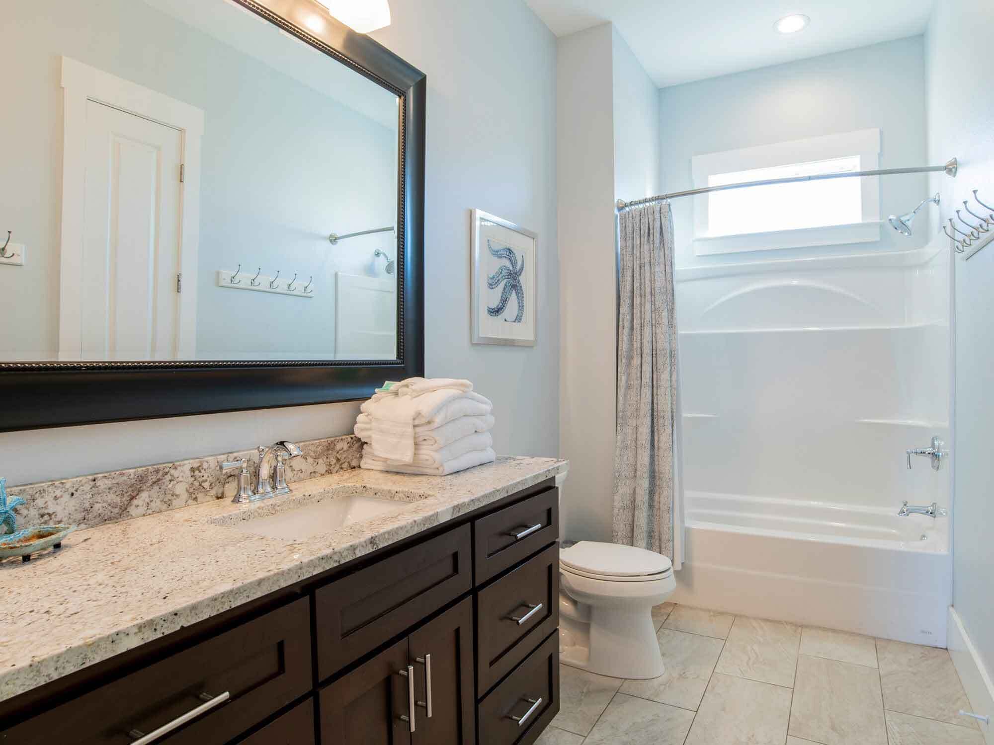 A modern bathroom with a marble sink, dark cabinetry, a white toilet, and a glass-enclosed shower.