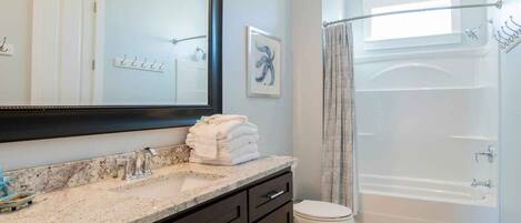 A modern bathroom with a marble sink, dark cabinetry, a white toilet, and a glass-enclosed shower.