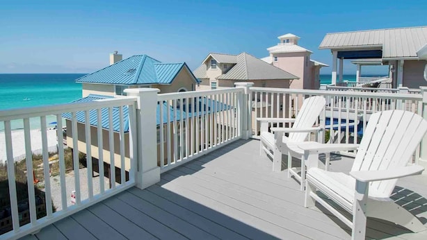 A deck with white railings overlooking a beach, featuring two Adirondack chairs and a covered seating area. - Magnolia House by Southern Vacation Rentals (Santa Rosa Beach)