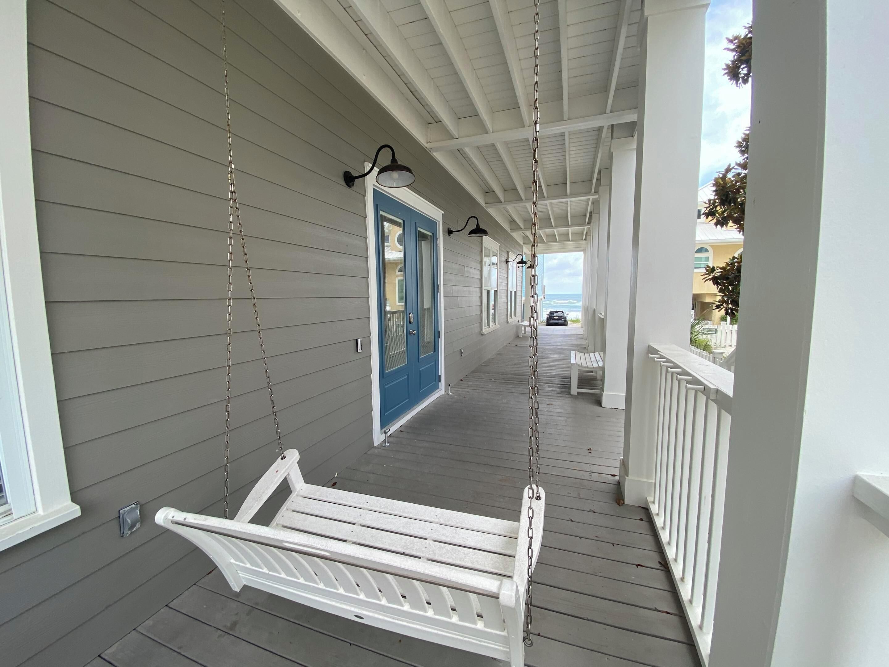 A covered porch with a white swing, a blue door, and a view of the ocean.