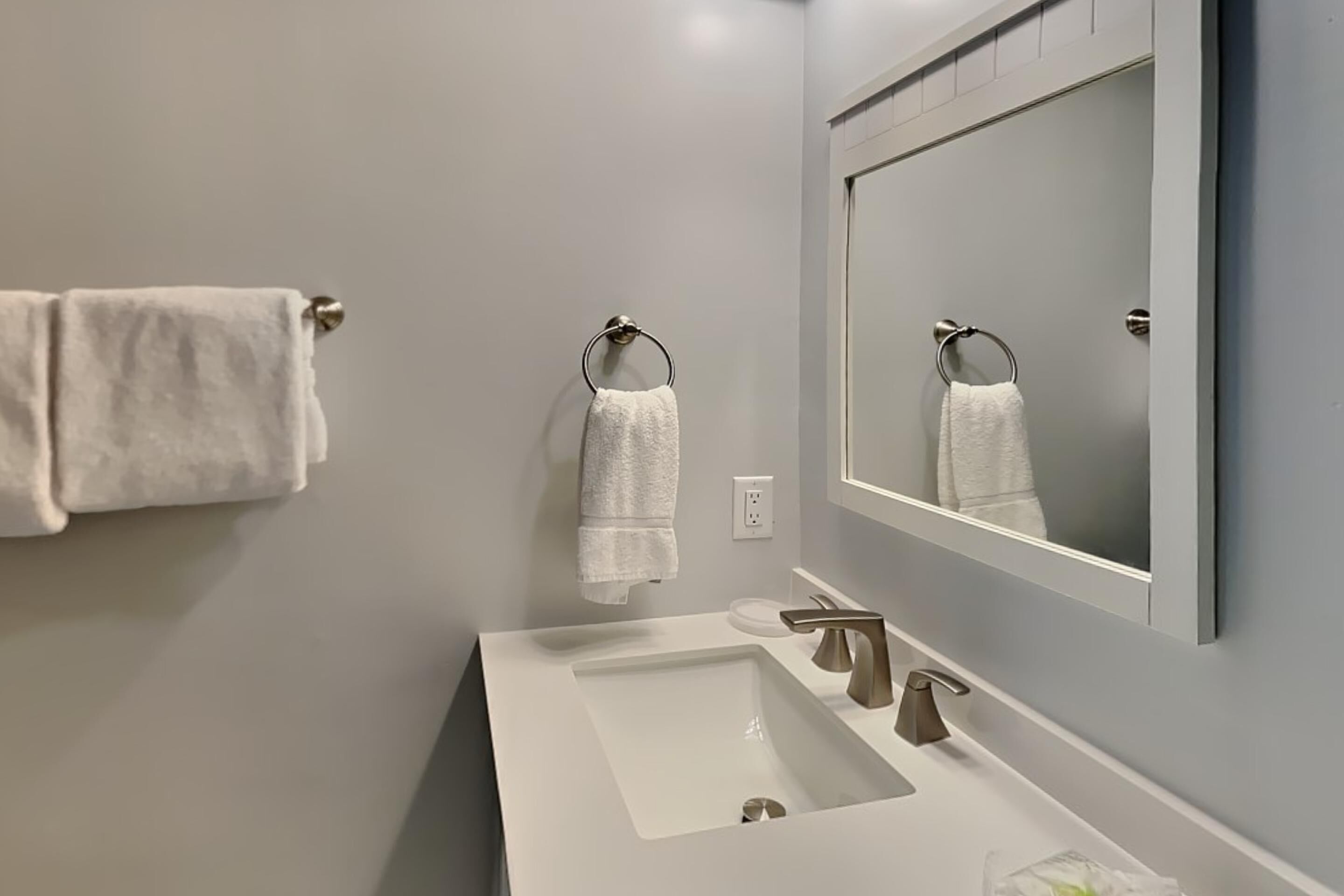 Une salle de bain moderne avec un lavabo blanc, deux robinets et un grand miroir.