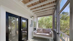 A covered porch with a cushioned seating area, a black door, and a 'hello' mat. - Happy as a Clam by Southern Vacation Rentals (Santa Rosa Beach)