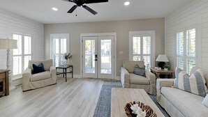 A spacious living room with a ceiling fan, two sofas, a coffee table, and a door leading to an outdoor area. - Happy as a Clam by Southern Vacation Rentals (Santa Rosa Beach)