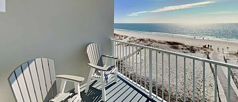 A balcony with two Adirondack chairs overlooking a beach.