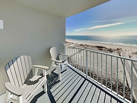 A balcony with two Adirondack chairs overlooking a beach.