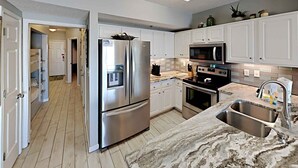 A modern kitchen with white cabinets, stainless steel appliances, a marble countertop, and a built-in microwave. - Tropic Isle #403 by Southern Vacation Rentals (Gulf Shores)
