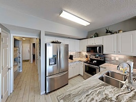 A modern kitchen with white cabinets, stainless steel appliances, a marble countertop, and a built-in microwave.