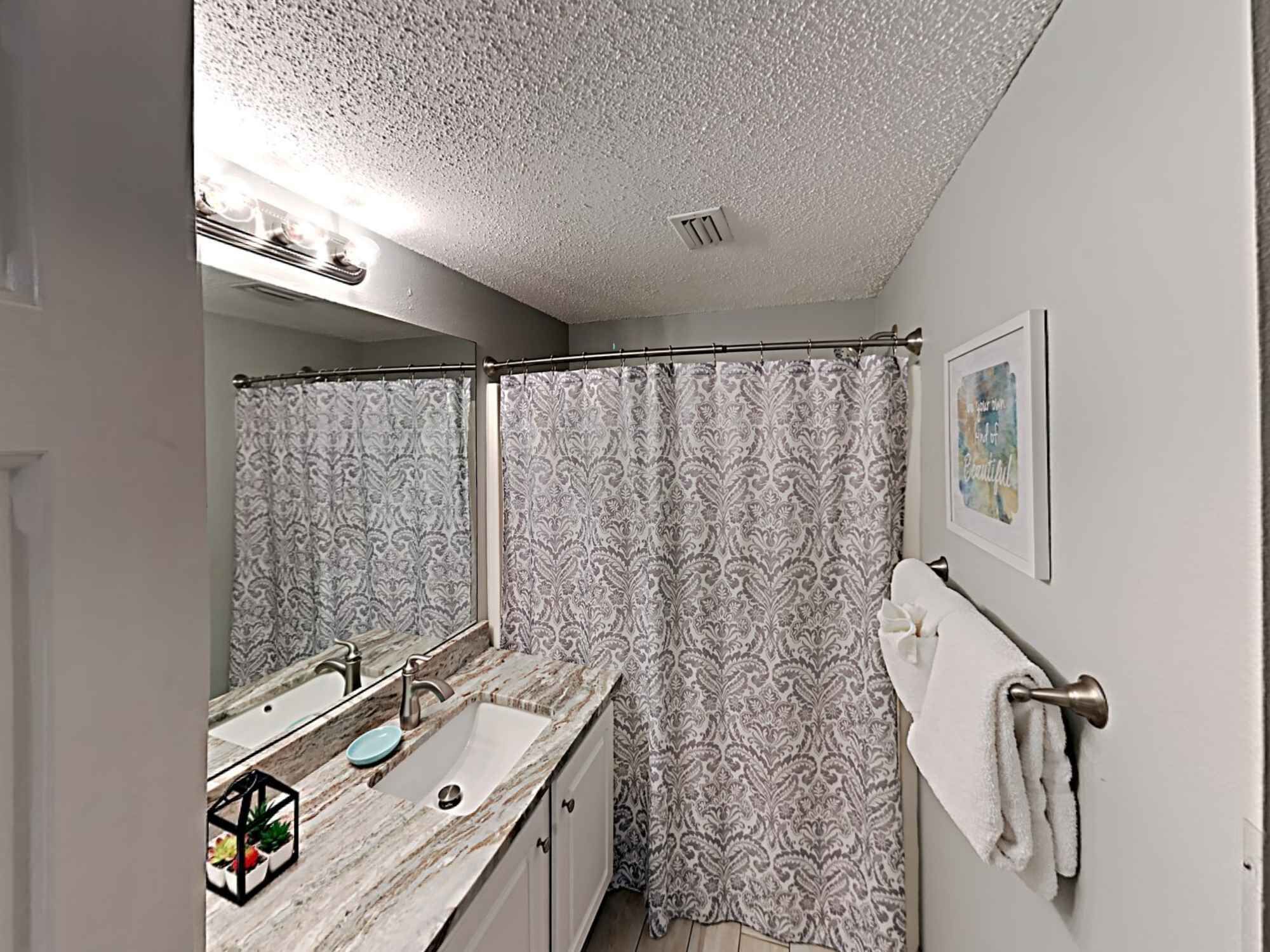 Un baño con lavamanos de mármol, cortina de ducha, toallero y un cuadro en la pared.