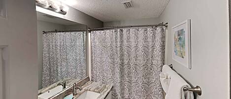 A bathroom with a marble sink, a shower curtain, a towel rack, and a framed picture on the wall.