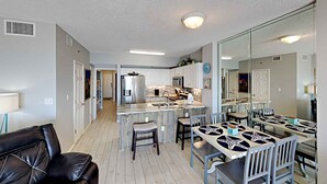 A modern kitchen with white cabinets, a stainless steel refrigerator, and a central island with bar stools. - Tropic Isle #403 by Southern Vacation Rentals (Gulf Shores)