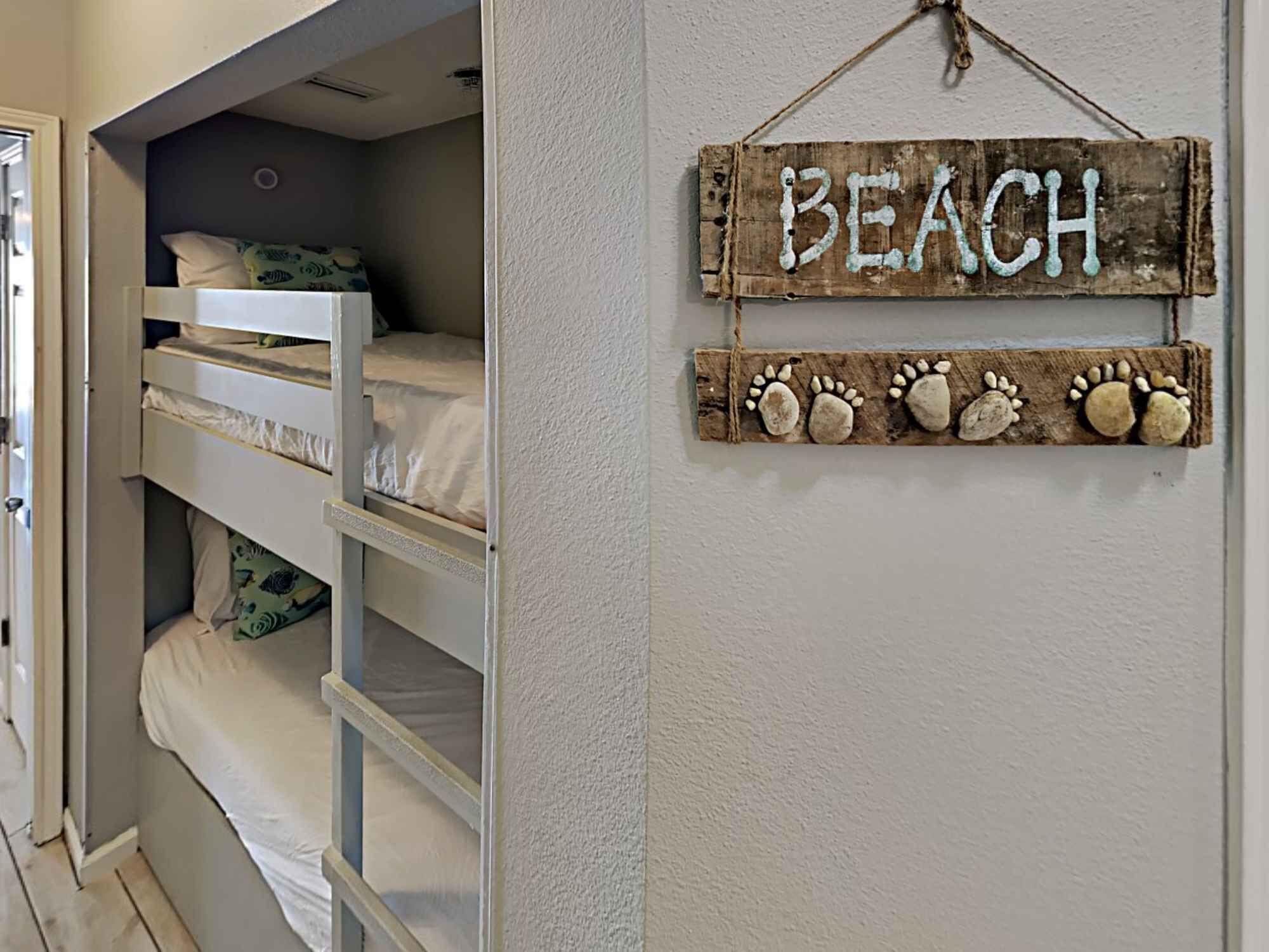 A bunk bed room with a 'BEACH' sign and a decorative paw print shelf.