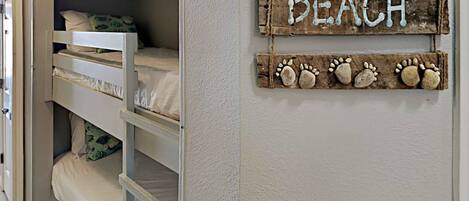 A bunk bed room with a 'BEACH' sign and a decorative paw print shelf.