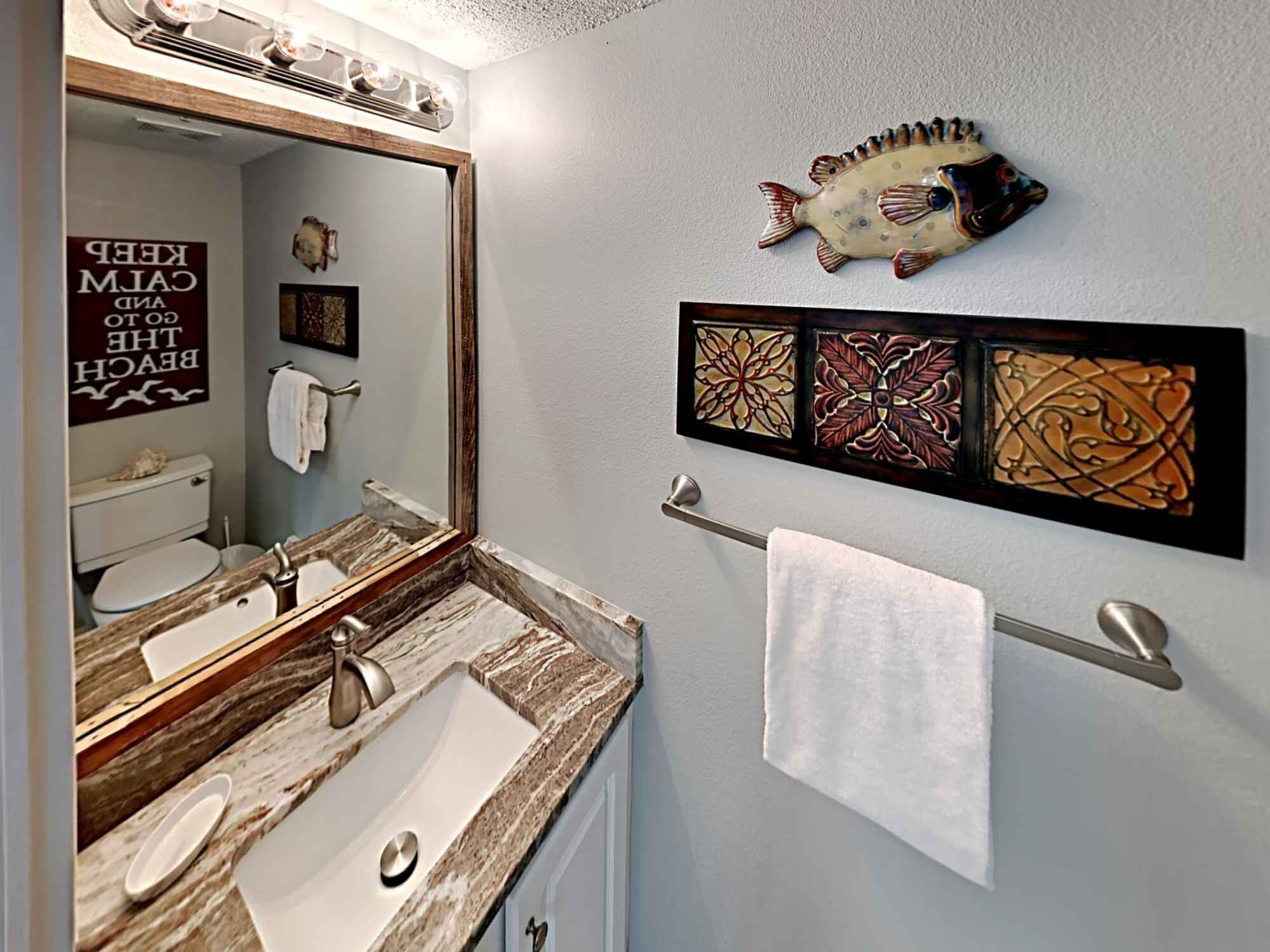 Une salle de bain avec un double lavabo, un porte-serviettes, une décoration murale représentant des poissons et une citation inspirante sur le mur.