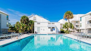 A swimming pool with a depth of 18 feet, surrounded by white buildings with balconies and palm trees. - Cotton Bayou Condominiums by Southern Vacation Rentals (Orange Beach)
