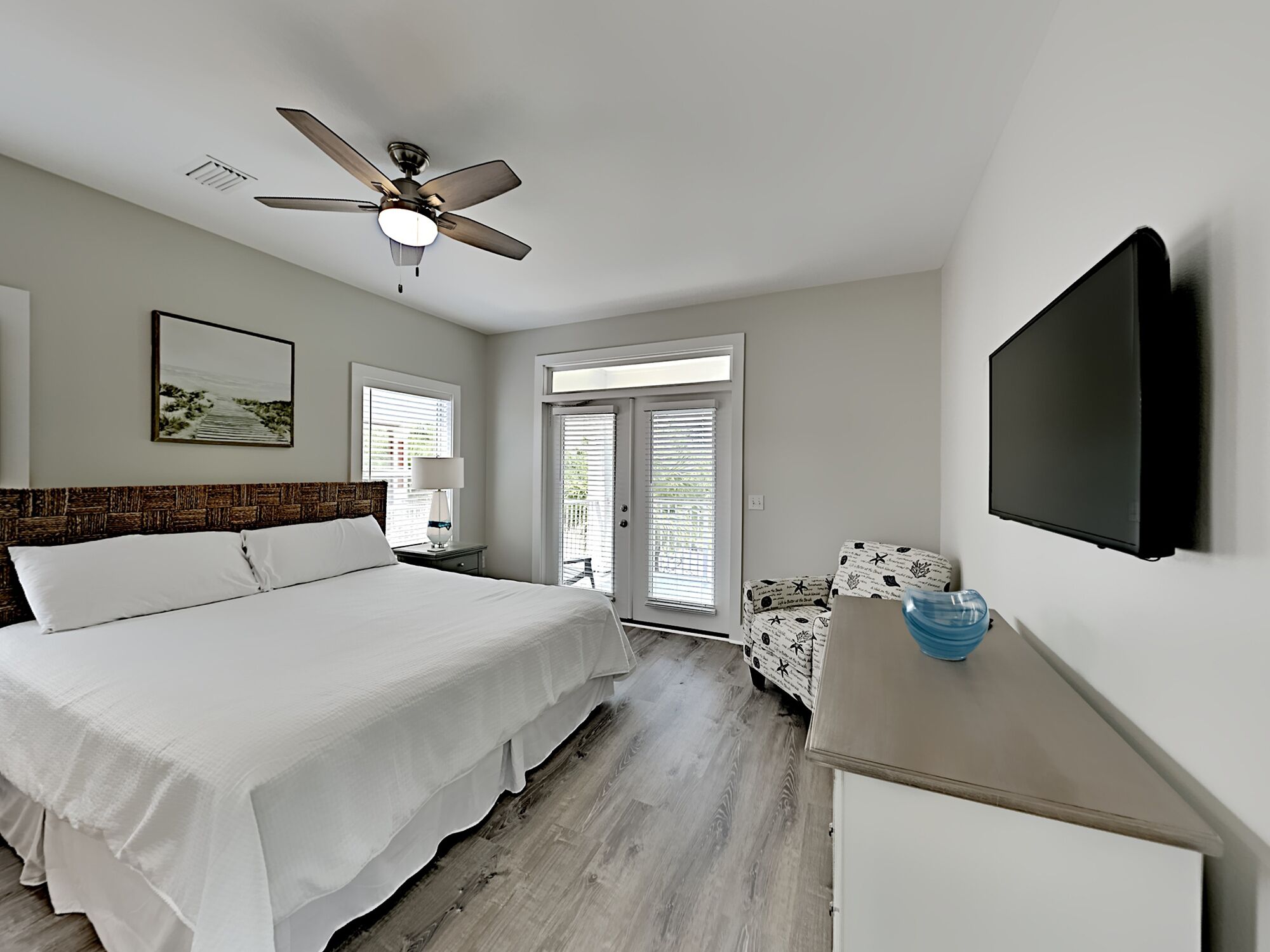 A bedroom with a bed, a ceiling fan, a TV mounted on the wall, and a window with blinds.