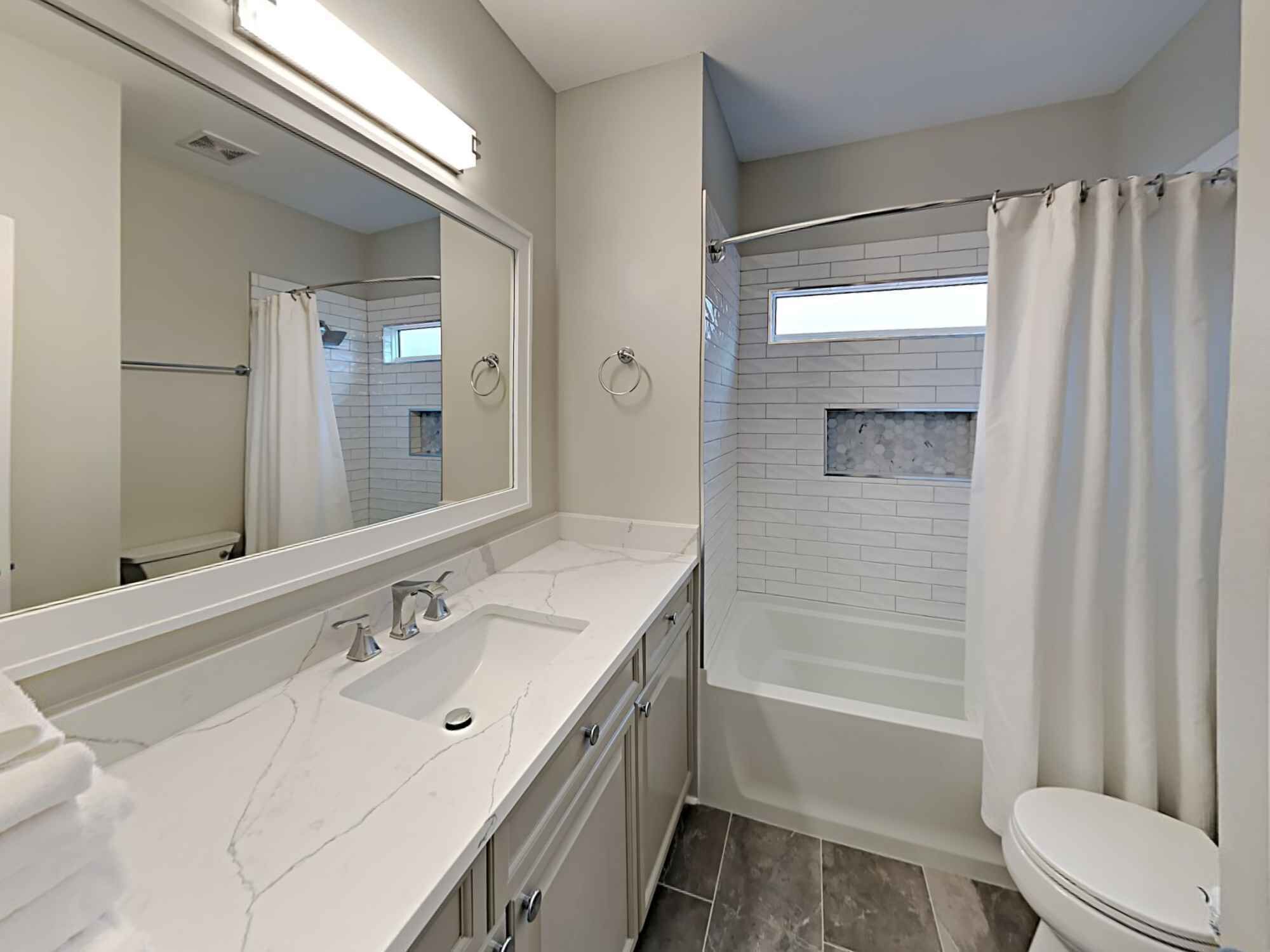 A bathroom with a large mirror, a sink, a toilet, and a bathtub.