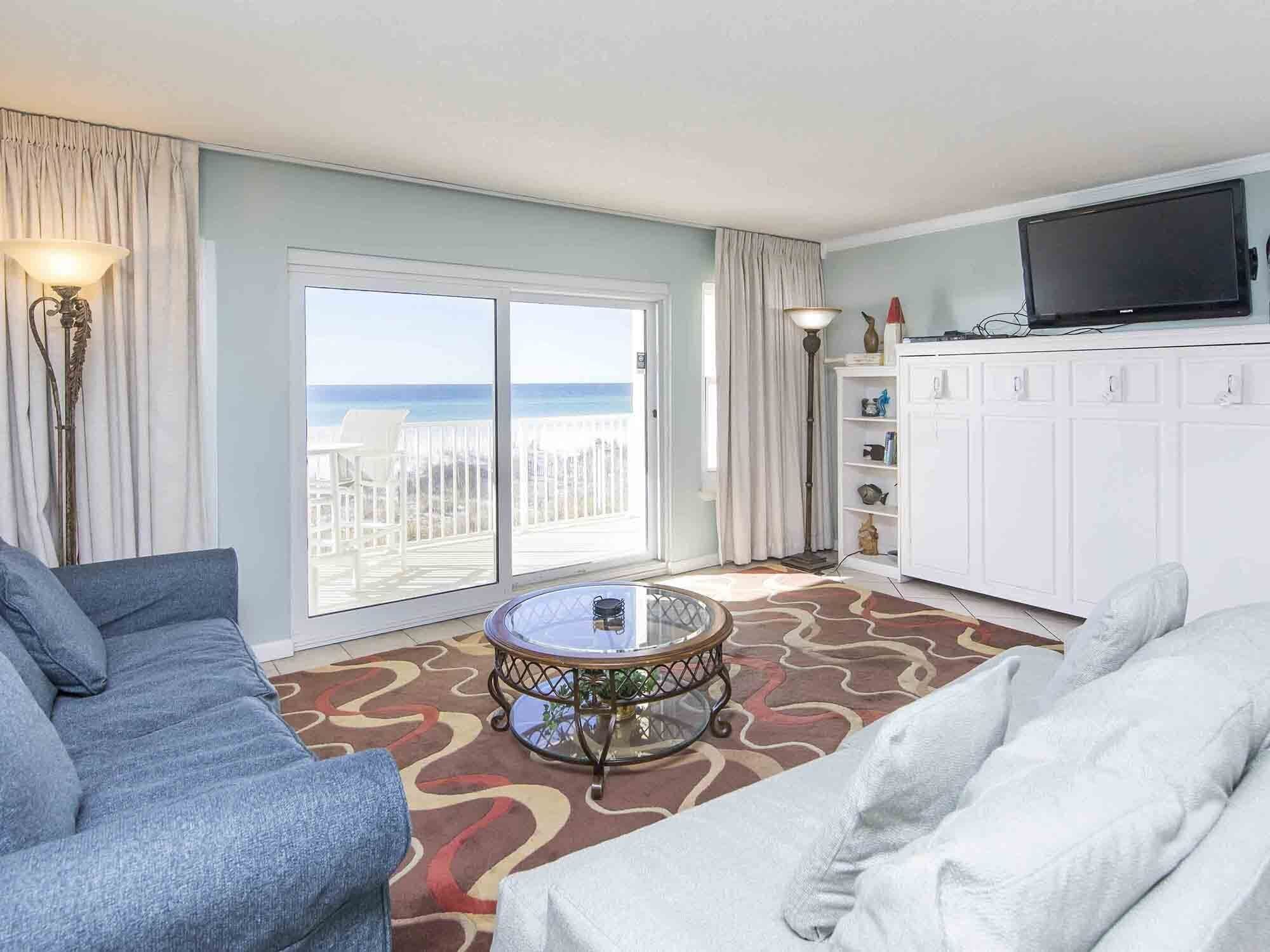 Et hotelværelse med balkon, sofa, spisebord og fjernsyn.