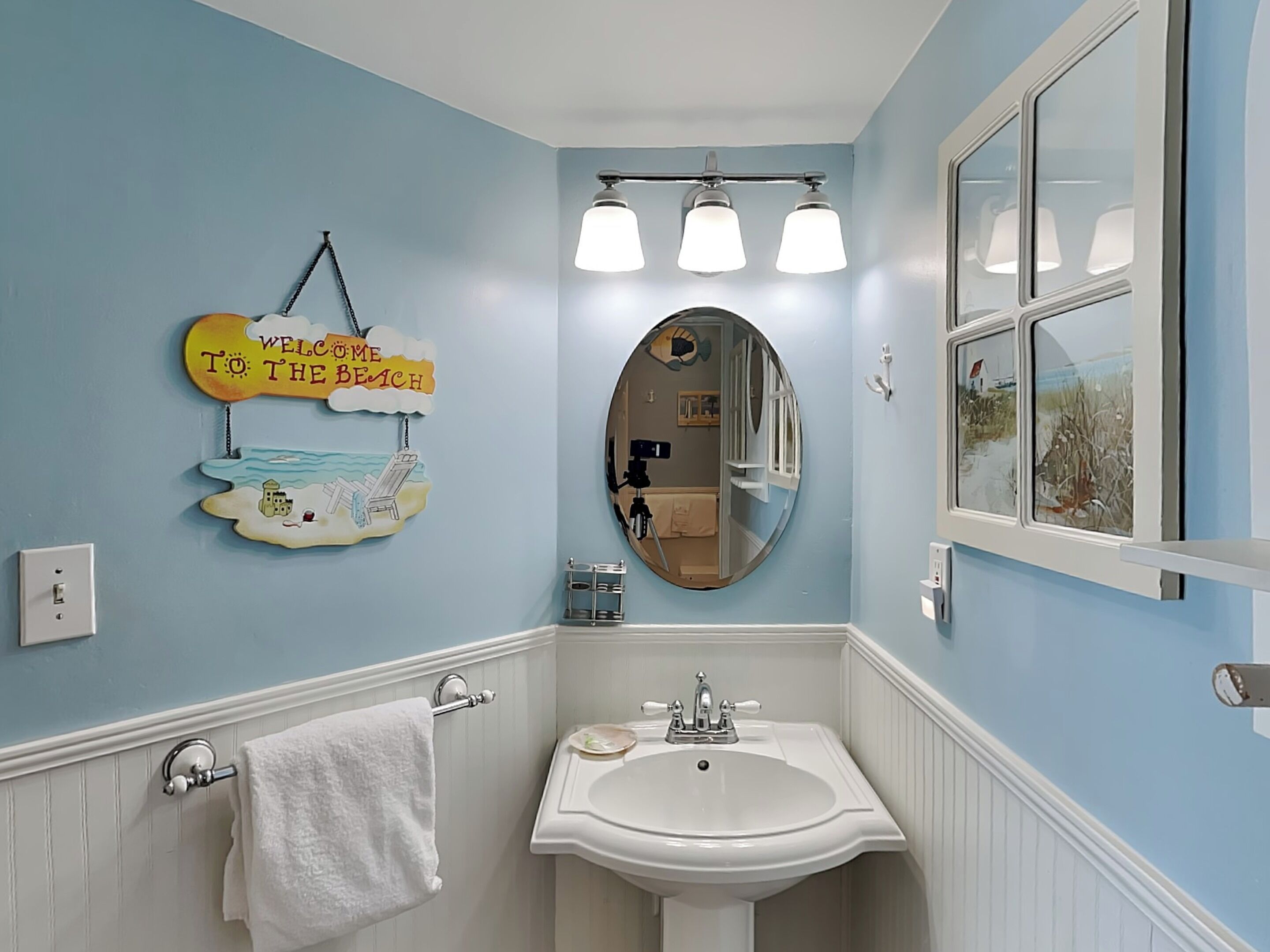 Une salle de bain avec un lavabo, un miroir et une pancarte indiquant « Bienvenue à la plage ».