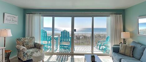 Un salon avec vue sur la plage, comprenant un canapé, des fauteuils, une table basse et un tapis.
