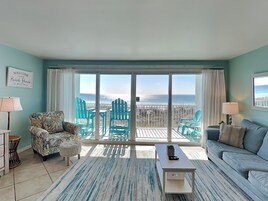 A living room with a view of the beach, featuring a sofa, chairs, a coffee table, and a rug.