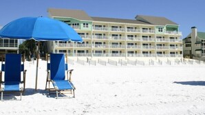 Ein Strandhotel mit mehreren Balkonen, einem Sandstrand und blauen Liegestühlen.