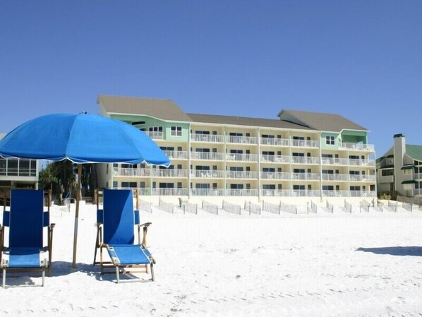 A beachfront hotel with multiple balconies, a sandy beach, and blue beach chairs. - Cabana Club by Southern Vacation Rentals (Destin)