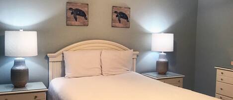 Quarto com uma cama, duas mesas de cabeceira, duas luminárias e duas obras de arte de tartarugas nas paredes.