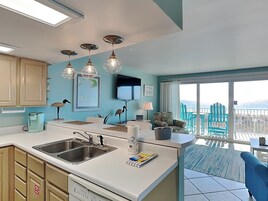 A modern kitchen with a large island, a built-in dishwasher, and a dining area with a view of the balcony.