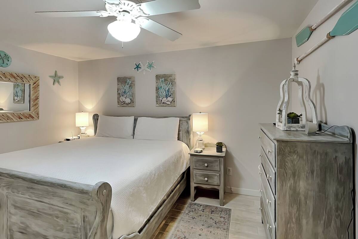 A bedroom with a bed, nightstands, a dresser, a ceiling fan, and wall art.