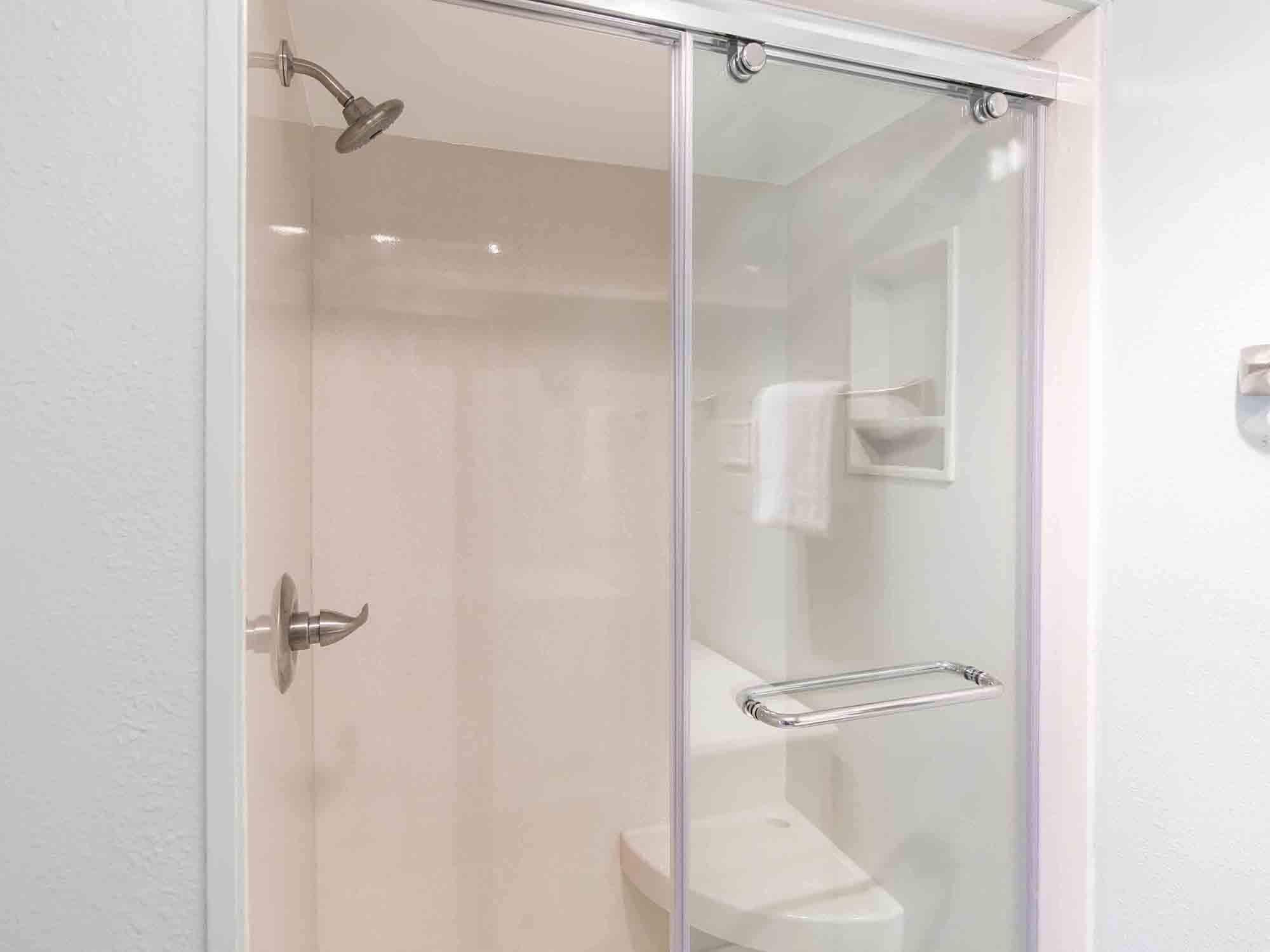A glass-enclosed shower with a handheld showerhead, a towel rack, and a toilet visible through the glass.