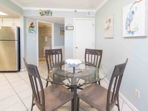 A dining area with a glass table surrounded by four chairs, a kitchen with a stainless steel refrigerator, and a door leading to another room. - Cabana Club by Southern Vacation Rentals (Destin)