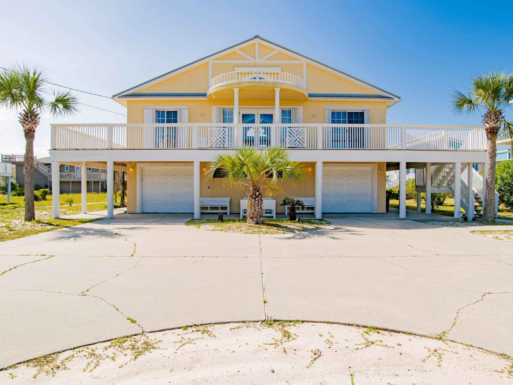 A two-story house with a balcony, garage doors, and palm trees.