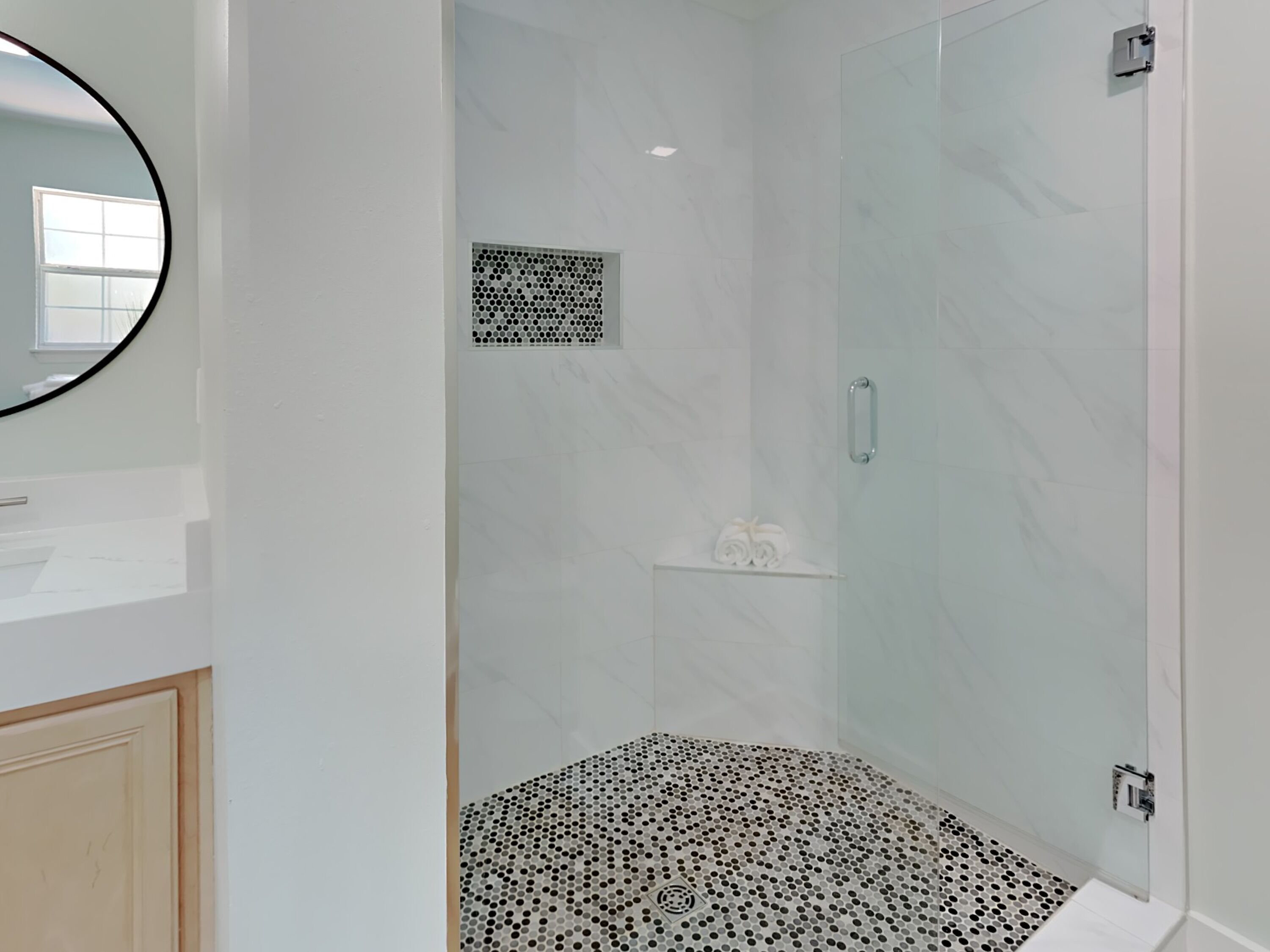 A modern bathroom with a glass shower enclosure, a white marble floor, and a small shelf with towels.