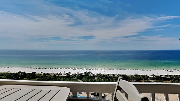 Blick auf einen Strand vom Balkon aus, mit Pool und Liegestühlen.