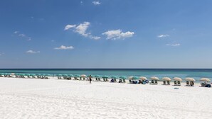 Ein Strand mit Reihen von Sonnenschirmen und Liegestühlen, einem klaren Himmel und einem ruhigen Meer.