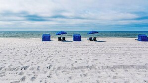 Una playa con varias sombrillas azules y sillas reclinables.