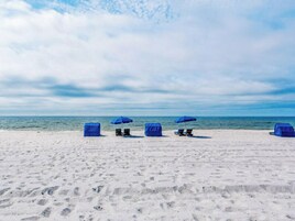 A beach with several blue beach umbrellas and lounge chairs.