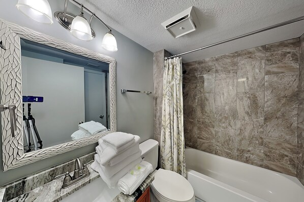 A bathroom with a marble sink, a toilet, a bathtub, and a shower curtain. - Harbour Place #202 by Southern Vacation Rentals (Orange Beach)