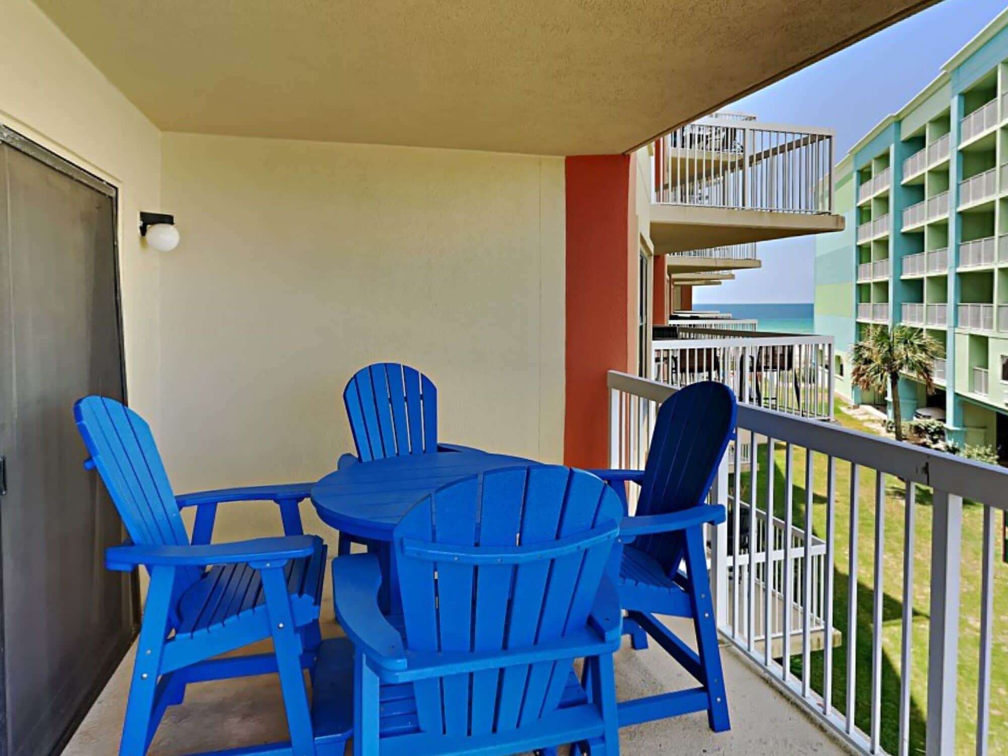 Un balcón con sillas Adirondack azules y vistas a un edificio con balcones y una palmera.