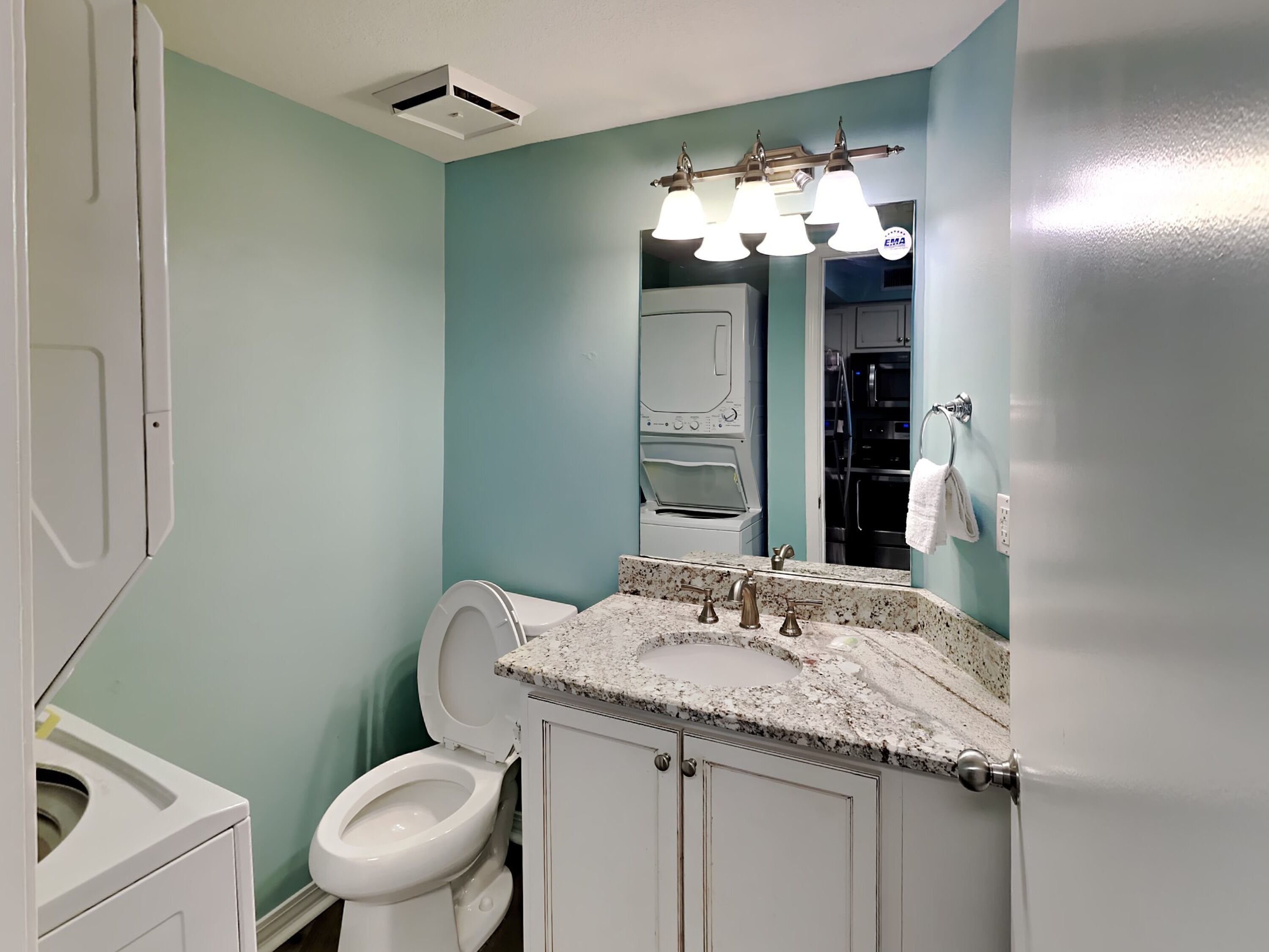 A bathroom with a white toilet, a granite countertop sink, and a mirror above it.