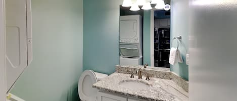 A bathroom with a white toilet, a granite countertop sink, and a mirror above it.