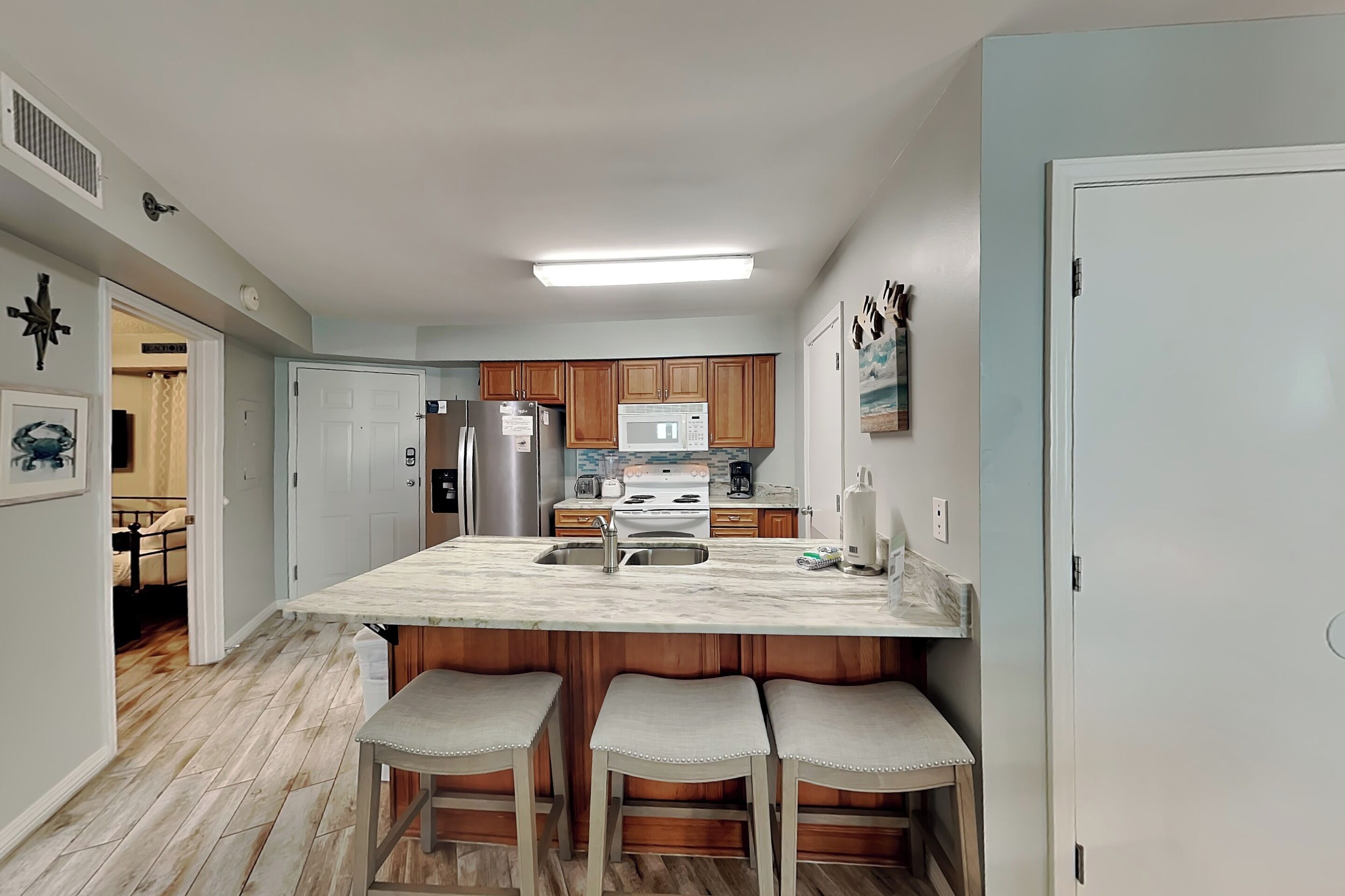 A modern kitchen with a central island, wooden cabinets, stainless steel appliances, and a bar stool seating area.