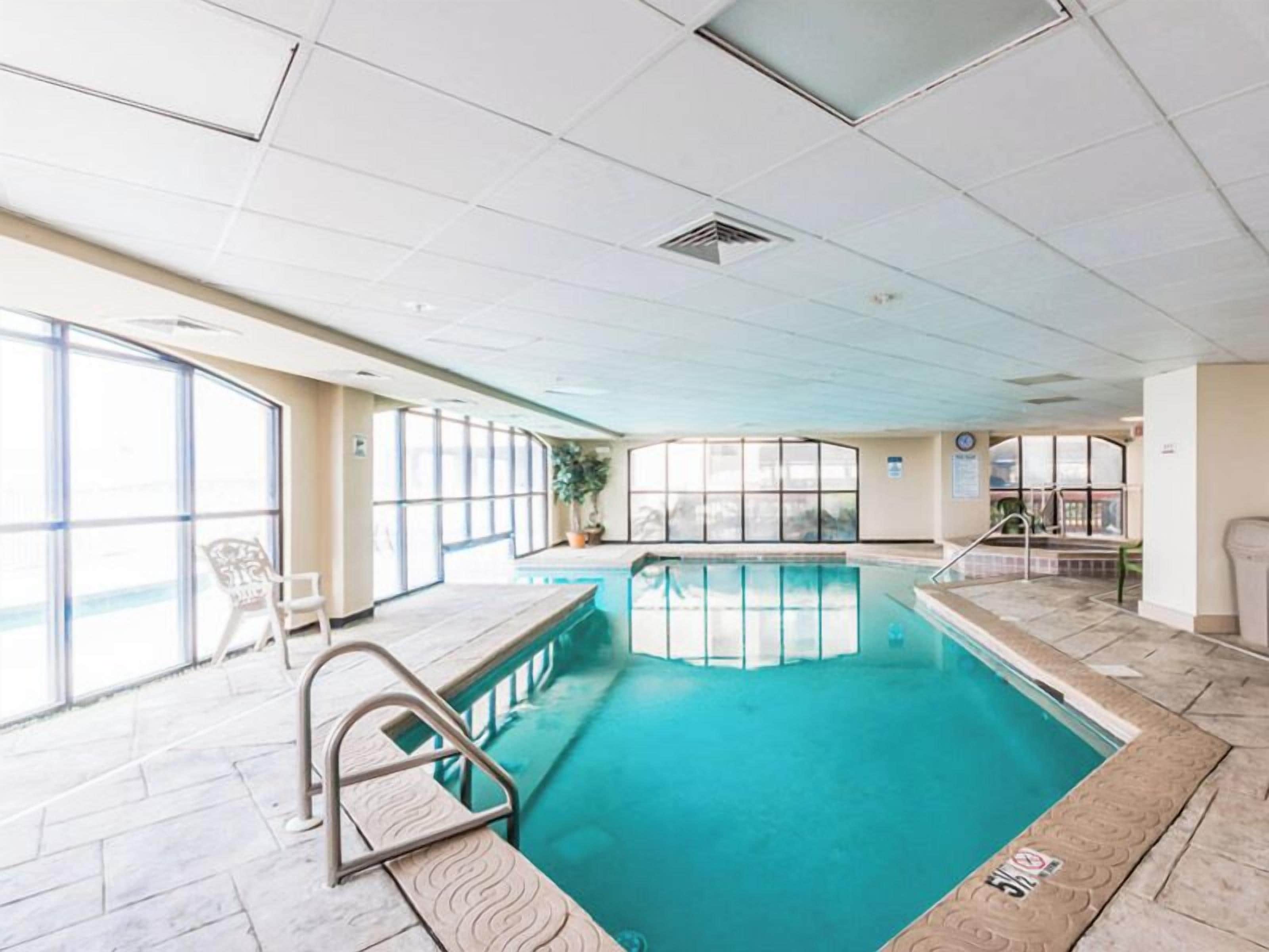 An indoor swimming pool with clear glass walls, a tiled floor, and a metal ladder.