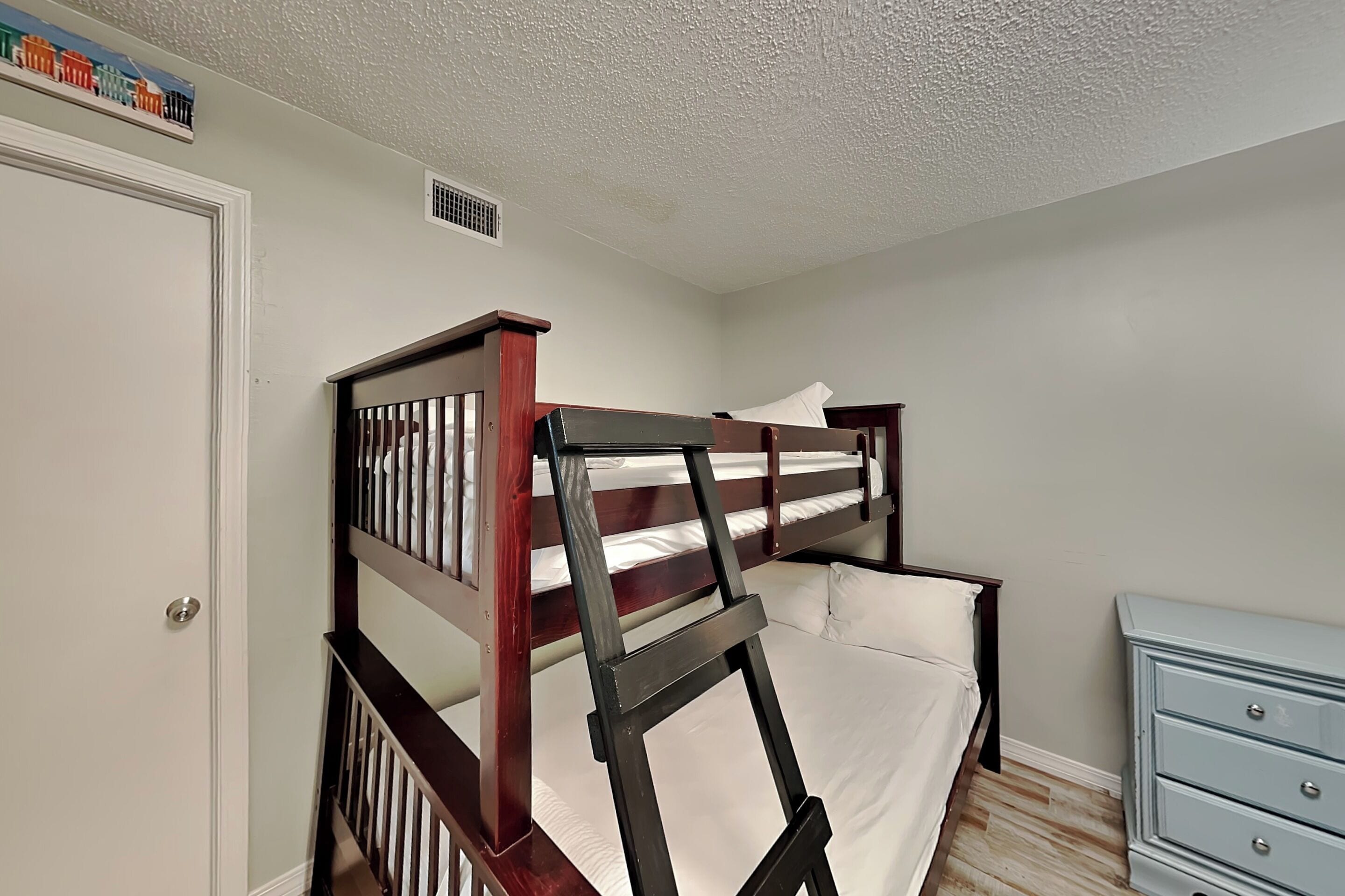 A bunk bed with a ladder, a dresser, and a door with a small vent.