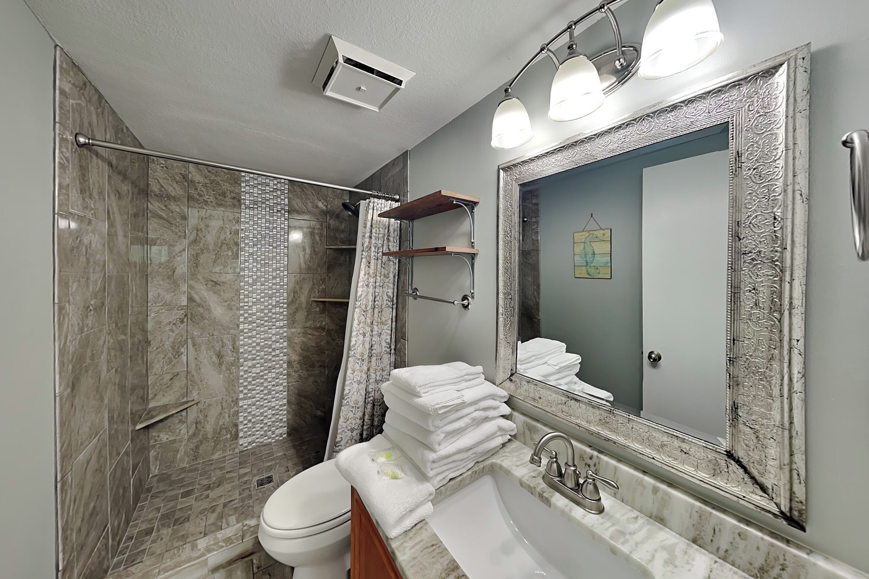 Un baño con ducha, inodoro, lavabo y un espejo grande.