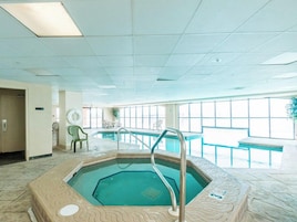 An indoor swimming pool with a tiled floor, a pool ladder, and a bench.