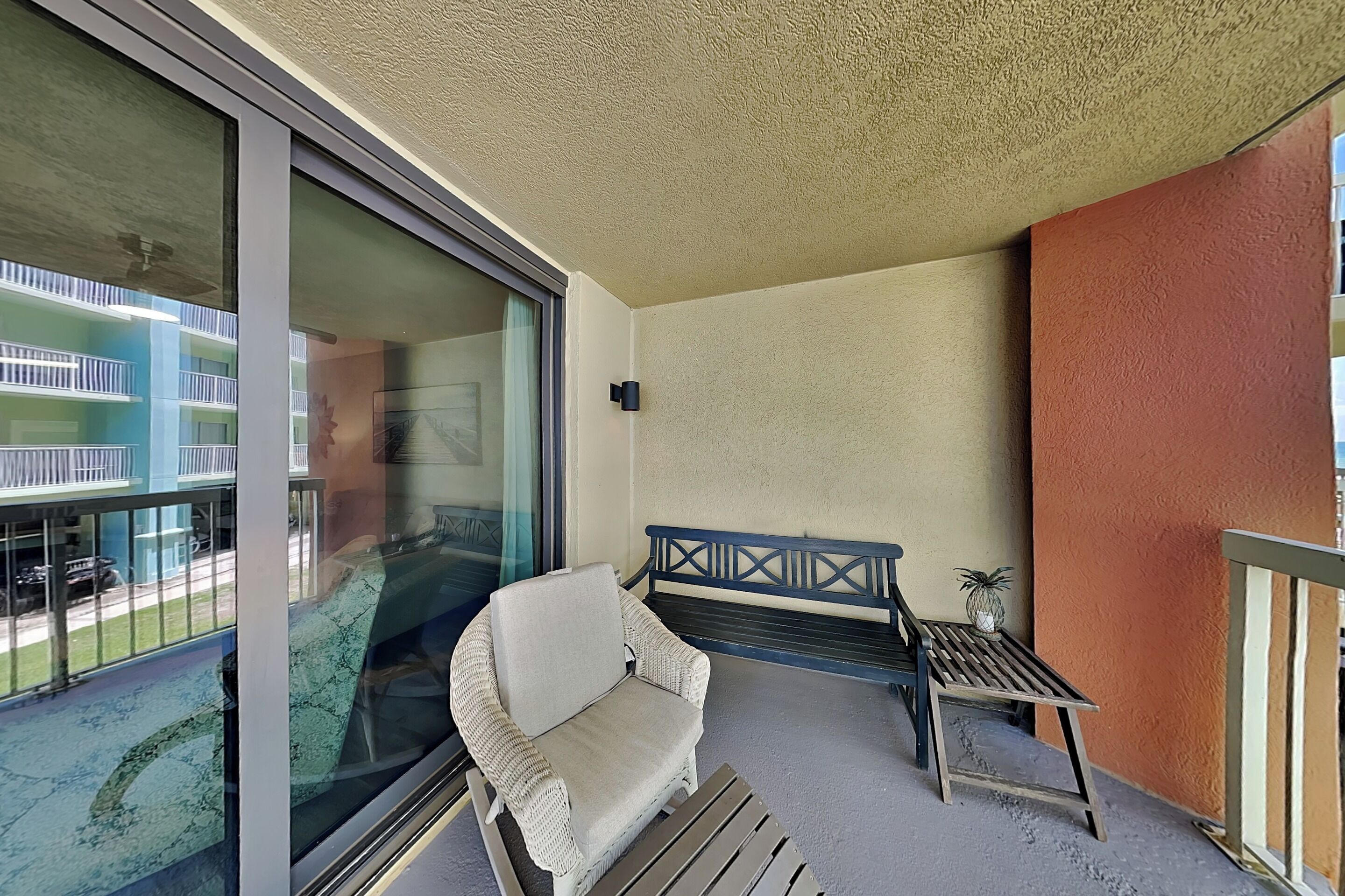 A balcony with a cushioned chair, a small table, and a bench.